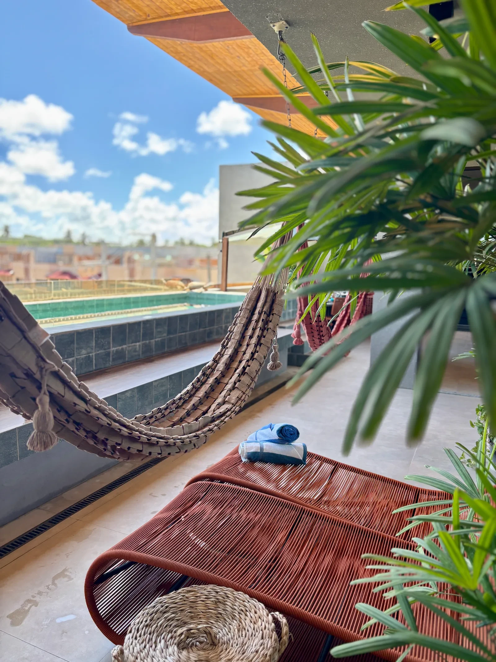 Rede armada à beira da piscina, à sombra das plantas.