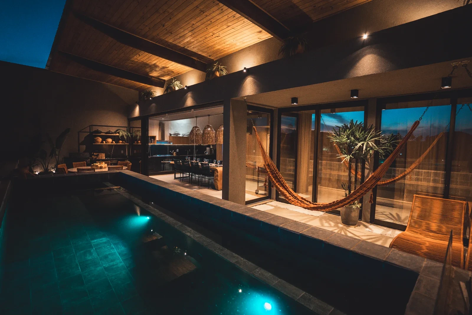 A piscina privativa ao anoitecer, com as redes e a área gourmet iluminada ao fundo.