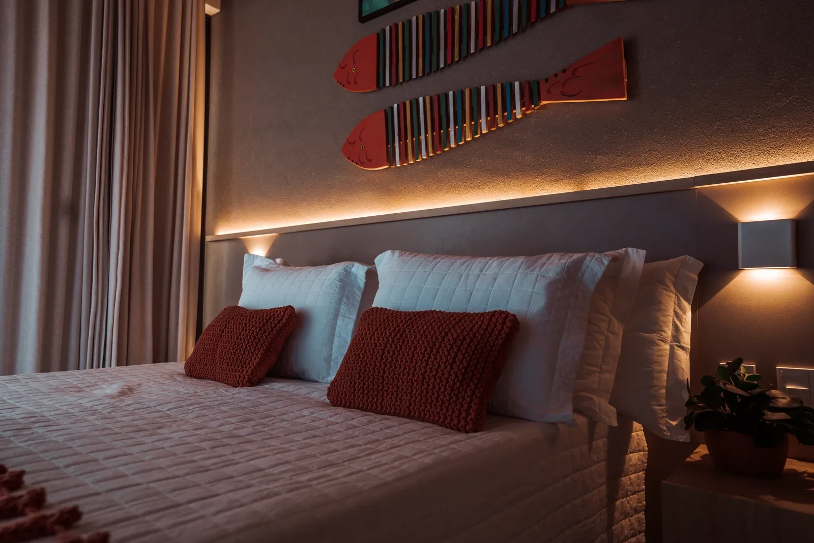 Cama de casal com almofadas e mantas, na suíte com cabeceira iluminada.