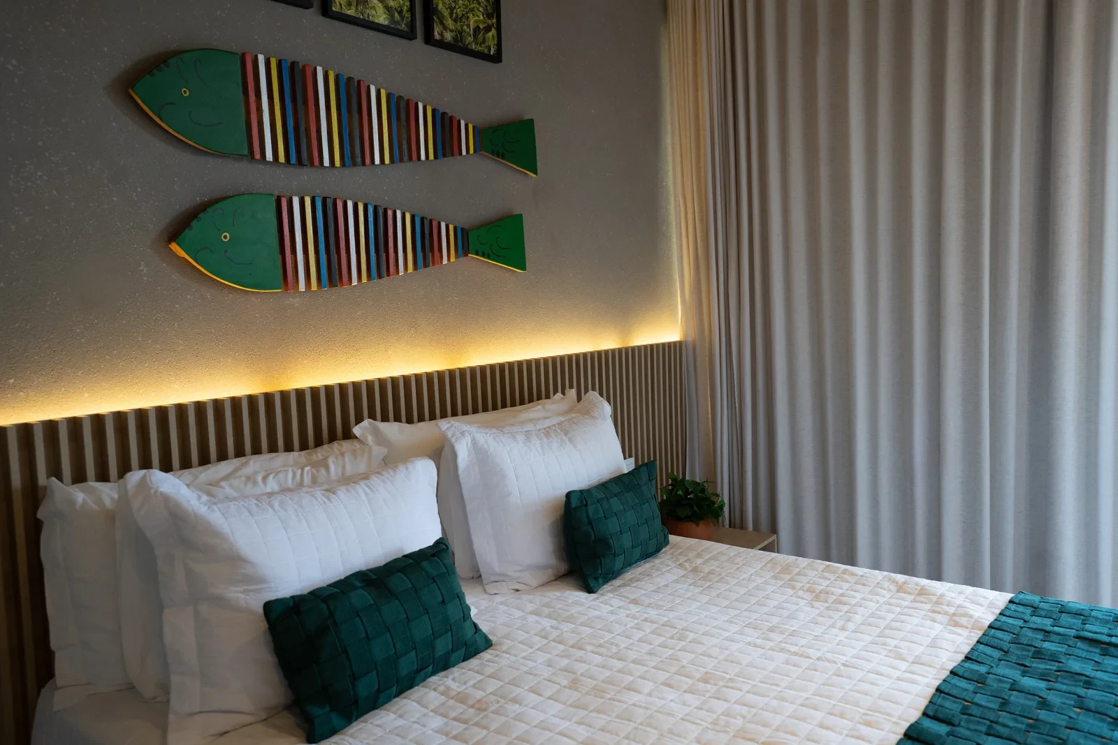 Cama de casal com roupa de cama branca e almofadas verdes.